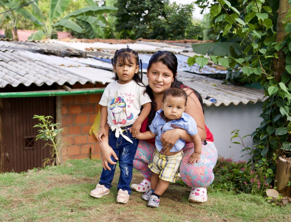 Madre colombiana con sus dos hijos frente a su casa, recibiendo transferencias de Renta Ciudadana